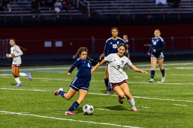 High school girls soccer players battling for the ball under the lights — sports action photography by Striide